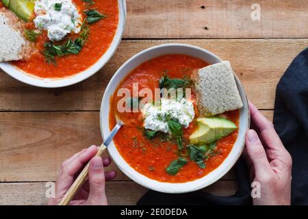 Draufsicht auf Ernte anonyme Person mit Anteil der hausgemachten Tomatensuppe in Schüssel auf Holztisch gelegt Stockfoto