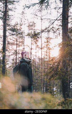 Seitenansicht der ruhigen weiblichen Reisenden in warmer Kleidung stehend Morgens in Nadelwäldern und im Winter die Natur genießen Stockfoto