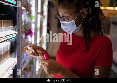 Afro latina junge Frau trägt eine Gesichtsmaske Shopping Make-up-Produkte Stockfoto