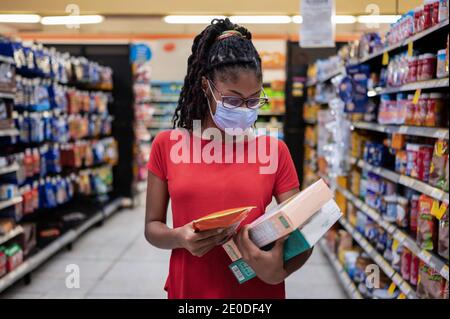 Afro latina junge Frau mit Gesichtsmaske geht Gang und schaut sich Produkte an, während sie im Supermarkt einkaufen Stockfoto