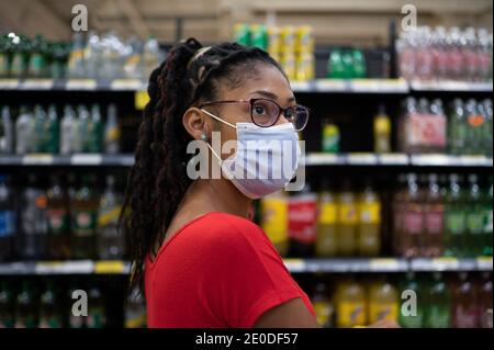 Afro latina junge Frau mit Gesichtsmaske sieht sich Produkte im Getränkegang an, während sie im Supermarkt einkauft Stockfoto