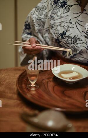 Nahaufnahme der Hände einer kaukasischen Frau im Kimono, die im Ryokan mit Essstäbchen japanisches Essen verzehrt Stockfoto