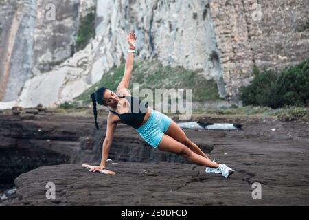 Entschlossene weibliche Sportlerin balanciert in der Seitenplanke während der Übungen Während des Trainings am Meer Stockfoto