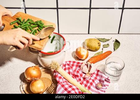 Von oben der Ernte unkenntlich weibliche Zugabe gehackte grüne Bohnen In den Topf während der Zubereitung gesunder Suppe mit Zwiebeln Kartoffelkarotte Und Knoblauch in Stockfoto