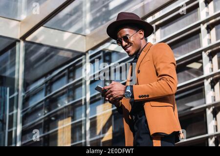 Inhalt African American männlich in trendigen Hut und Kleidung zu Fuß Entlang der städtischen Straße und Surfen Handy Stockfoto