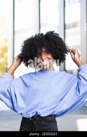 Fröhliche junge afroamerikanische Frau mit lockigen Haaren zu suchen Kamera auf der Straße stehen Stockfoto