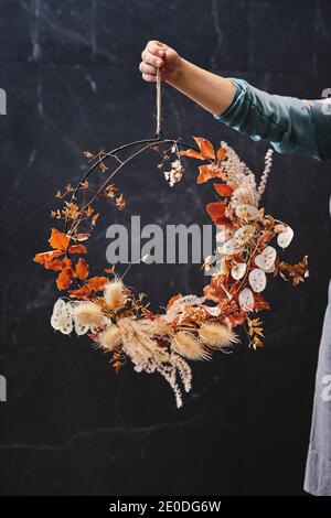 Unkenntlich weibliche Floristin stehend mit Blumenkranz aus getrocknet Blätter und rote Hortensien Blumen auf schwarzem Hintergrund im Studio Stockfoto