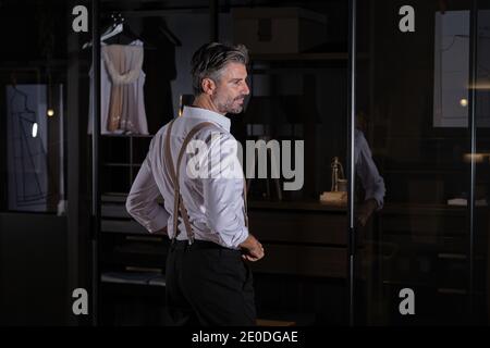 Stock Foto von eleganten Mann mittleren Alters tragen Anzug und Hosenträger lächelnd und Blick auf die Seite. Stockfoto