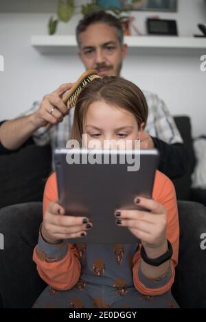 Liebevolle vorsichtig Erwachsene Papa mit Haarbürste kämmende Haare der Tochter Tablet zu Hause verwenden Stockfoto