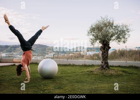 Flexibler Mann in activewear lehnt auf fit Bälle und tun Yoga in Camatkarasana auf grünem Rasen während Pilates Training Stockfoto