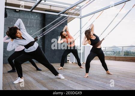 Gruppe von Menschen in Sportbekleidung, die sich auf Riemen lehnen und üben Yoga in Parivrtta Adho Mukha Svanasana auf Holzterrasse Stockfoto