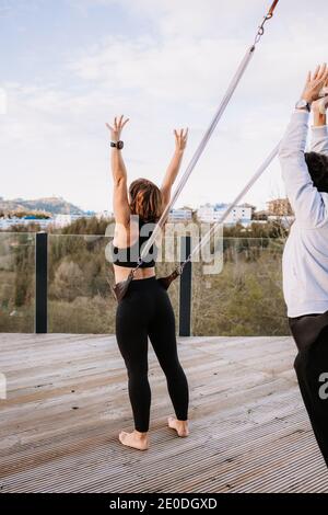 Rückansicht der Gesellschaft von Menschen in aktivewear, die sich darauf stützen Gurte und Yoga in Urdhva Hastasana mit erhobenen Armen Auf der Terrasse Stockfoto