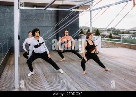 Gruppe von Menschen in Sportbekleidung, die sich auf Riemen lehnen und üben Yoga in Parivrtta Adho Mukha Svanasana auf Holzterrasse Stockfoto