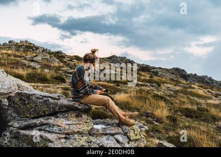 Seitenansicht der weiblichen Touristen, die auf rauem Felsen sitzen und Mit dem Smartphone beim Wandern in den Bergen entspannen Stockfoto