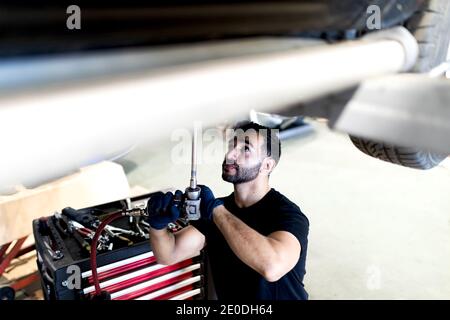 Beschäftigte männliche Techniker mit Spezialinstrument und Befestigung Auto während Arbeiten in modernem Service Stockfoto