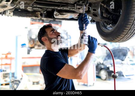 Beschäftigte männliche Techniker mit Spezialinstrument und Befestigung Auto während Arbeiten in modernem Service Stockfoto