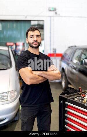 Serious männlichen Techniker in Handschuhen zu Fuß mit Werkzeugschrank in Moderner Autoservice Stockfoto