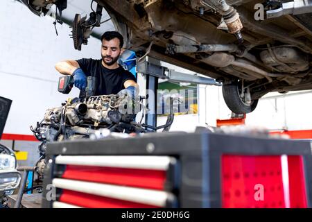 Niedriger Winkel der fokussierten männlichen Mechaniker mit elektrischen Schraubendreher Befestigung Motor des Autos während der Arbeit im Service Stockfoto