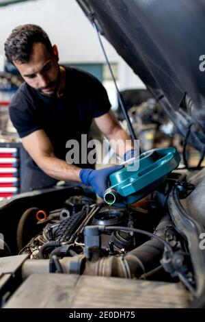 Serious männlich Mechaniker Gießen Motoröl in Motor des Autos Während der Arbeit im Reparaturservice Stockfoto