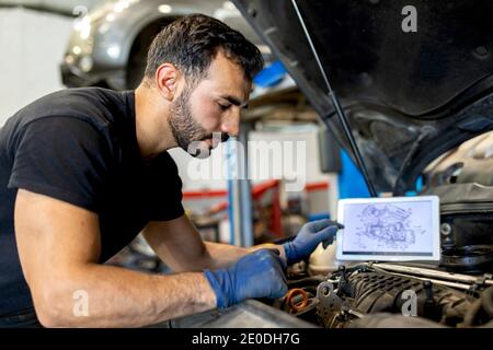 Seitenansicht des männlichen Technikers mit Motorschema Tablet-Überprüfung Auto-Motor während der Diagnose im modernen Service Stockfoto