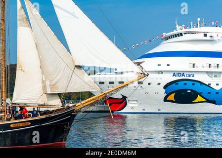 Ein Kreuzfahrtschiff der AIDA Cruises im Hafen von Kiel zu Gast, begleitet von einem Segelschiff mit gesetztenSegeln Stockfoto