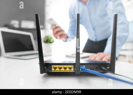 Wireless Router mit drei Antennen und Kabel angeschlossen. Mann mit Smartphone im Hintergrund Stockfoto