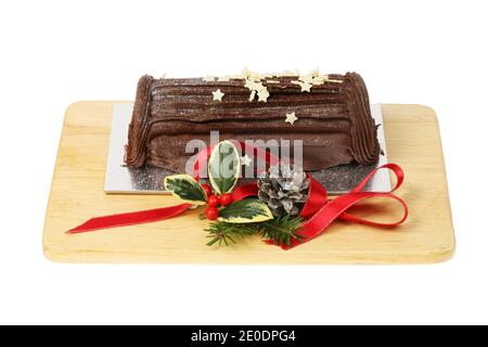 Schokolade Yule Log auf einem Holzbrett mit saisonalem Laub und rotem Band, isoliert gegen weiß dekoriert Stockfoto