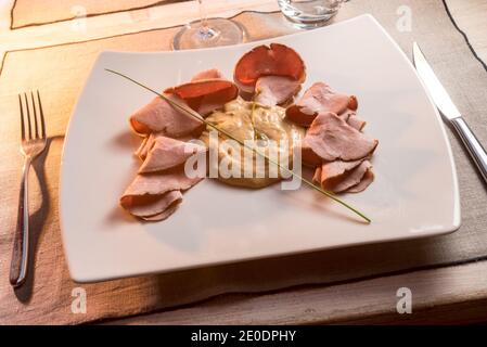 Vitello tonnato, typisch italienisches Roastbeef mit eingelegten Kapern, Kalbsscheiben, Mayonnaise-Sauce mit Thunfisch in einem weißen Gericht auf einem Trattoria-Tisch Stockfoto