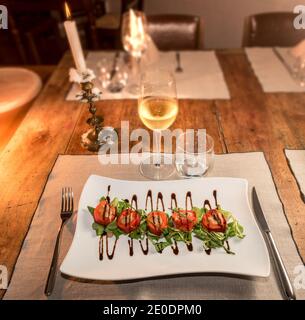 Gefüllte Pfefferrollen über Baldrian-Salat mit Balsamico-Essig in Weiße quadratische Platte auf rustikalen Tisch der italienischen Trattoria mit Kerze und Wein entzündet gla Stockfoto