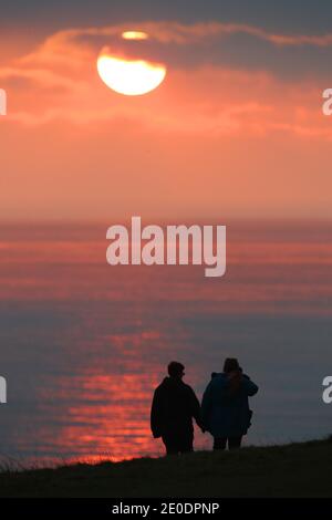 Cuckmere Haven, Seaford, Großbritannien. Dezember 2020. Die Sonne geht zum letzten Mal 2020 unter, während Wanderer die Aussicht von den Seven Sisters Cliffs in Sussex genießen.Quelle: James Boardman/Alamy Live News Stockfoto