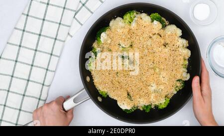 Bratpfanne mit Blumenkohl und Brokkoli gekrönt mit Alfredo-Sauce und Semmelbröseln in der Nähe in Frau Hände. Schritt für Schritt Gemüse Auflauf Rezept, Stockfoto