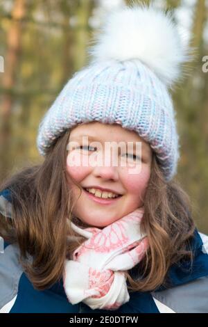 Junge Mädchen im Alter von 8, trägt einen Wolle / Wollbommel Hut, und Schal, während einer Familie Winter Spaziergang über West End Common, Esher, in Surrey, Großbritannien. (122) Stockfoto