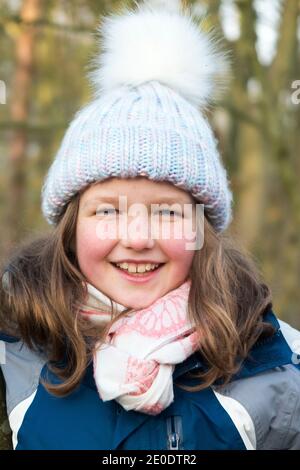 Junge Mädchen im Alter von 8, trägt einen Wolle / Wollbommel Hut, und Schal, während einer Familie Winter Spaziergang über West End Common, Esher, in Surrey, Großbritannien. (122) Stockfoto