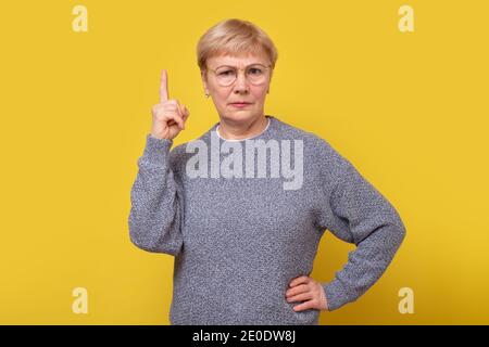 Ältere Frau zeigt nach oben und sieht wütend aus, zeigt die Richtung mit den Fingern an, gibt Ratschläge. Studioaufnahme Stockfoto