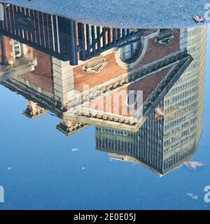 Alte und neue Gebäude spiegeln sich in Wasserpfütze in Die Straße Stockfoto