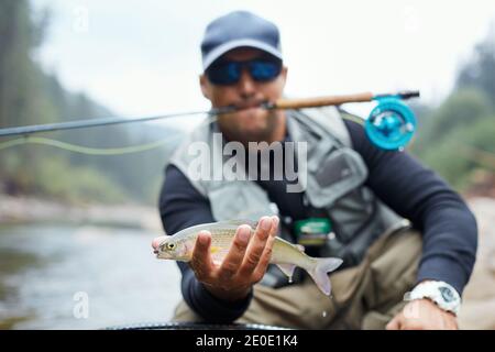 Portrait eines professionellen Fischers, der Regenbogenforelle im Gebirgsfluss zeigt. Glücklicher Mann hält seinen Fang während Lieblings-Hobby an der frischen Luft. Stockfoto