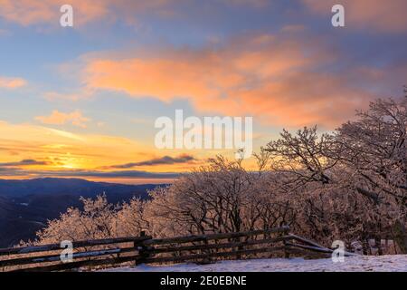 Devil's Knob Overlook – Sonnenuntergang über Blue Ridge Mountains mit Eisbedeckte Bäume und geteilter Schienenzaun im Vordergrund mit Rosa und lila Wolken Stockfoto