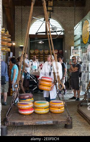 In De Waag, einem Käsewägehaus aus dem 17. Jahrhundert, stellt ein Mann ein paar Räder von Gouda Käse auf eine alte Skala. In diesem Gebäude befindet sich heute ein Käsemuseum. Stockfoto