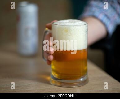 Männliche Hand hält große Tasse voll von kaltem frischen alkoholischen Bier auf Holzhintergrund, Mann zu Hause, selektive Fokus Stockfoto