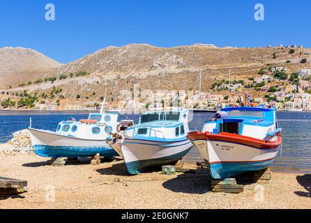 Drei Boote, die auf Holzständen in einem kleinen Bootshof auf Symi Island, Griechenland, angehoben wurden Stockfoto