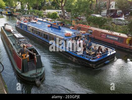 Die Electric Barge, ein Partyboot im Londoner Little Venice Basin, passiert ein schmales Boot auf dem Regent's Canal in London, England. Stockfoto