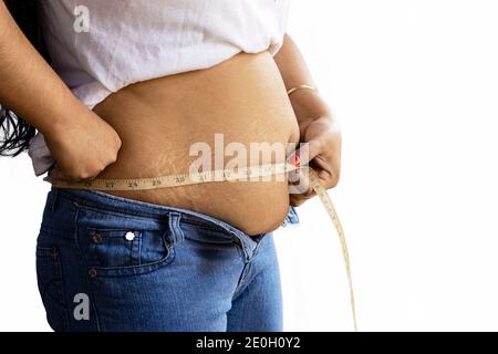 Mittlere Seitenansicht einer indischen Frau, die Fett misst Bauch mit Klebeband auf weißem Hintergrund Stockfoto