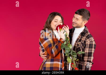 Romantisches Foto von einem schönen Paar auf einem roten Hintergrund. Ein Mann umarmt ein junges Mädchen, das glücklich mit einem Strauß Rosen steht. Hochwertige Fotos Stockfoto