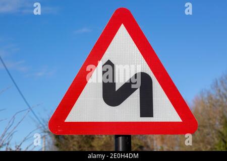 Rotes Dreieck Straßenschild Warnung vor scharfen Kurven voraus, Großbritannien Stockfoto
