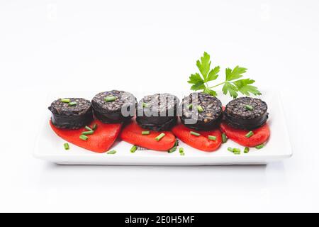 Spanische schwarze Pudding-Scheiben auf Piquillo-Paprika in weißer Platte auf weißem Hintergrund. Spanische Tapas. Stockfoto