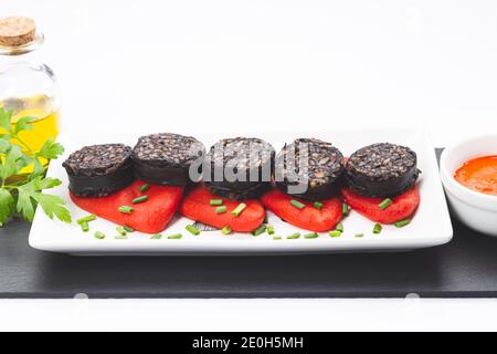 Spanische schwarze Pudding-Scheiben auf Piquillo-Paprika in weißer Platte auf weißem Hintergrund. Spanische Tapas. Stockfoto