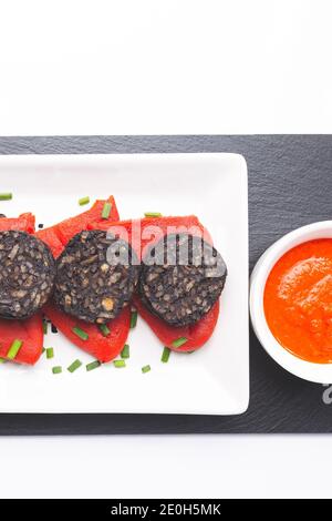 Spanische schwarze Pudding-Scheiben auf Piquillo-Paprika in weißer Platte auf weißem Hintergrund. Spanische Tapas. Stockfoto