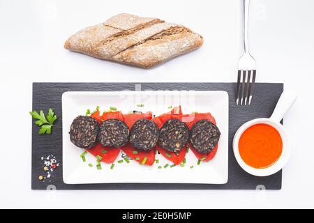 Spanische schwarze Pudding-Scheiben auf Piquillo-Paprika in weißer Platte auf weißem Hintergrund. Spanische Tapas. Stockfoto