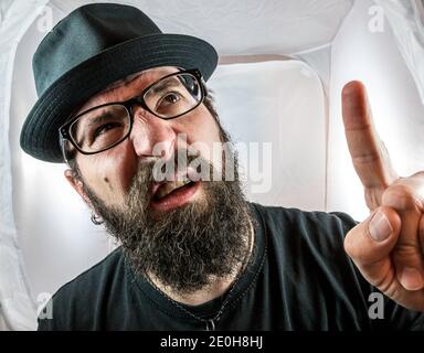 Ein bärtiger Mann mit schwarzer Brille und Hut, der Finger zeigt Und Fragen stellen Stockfoto