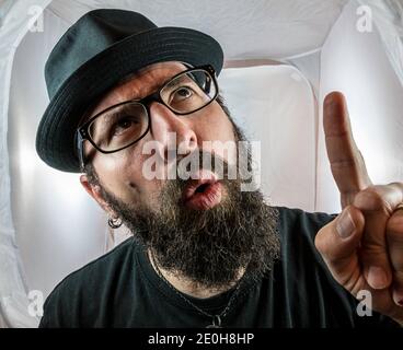 Ein bärtiger Mann mit schwarzer Brille und Hut, der Finger zeigt Und Fragen stellen Stockfoto